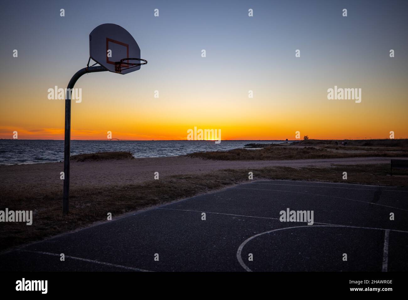Empty outdoor basketball court by a beach with a magnificent colorful sunset in the background