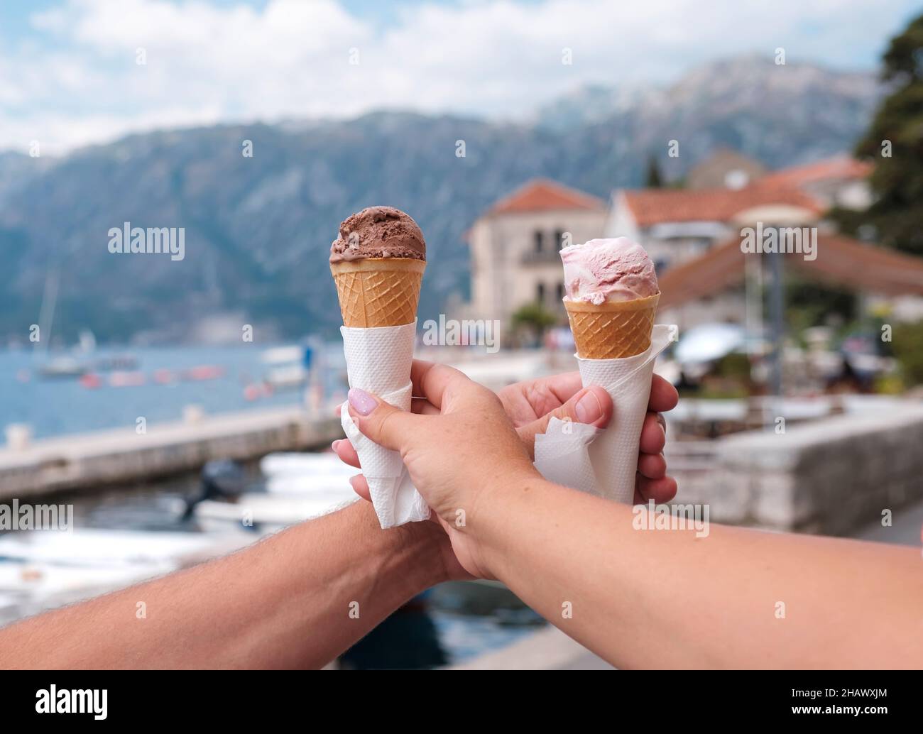 Female and male hand with ice cream in a cone on the background of the old town, Dobrota, Kotor, Montenegro, Europe Stock Photo