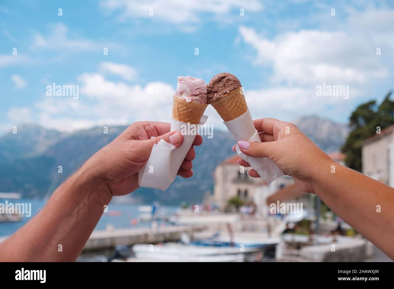 Female and male hand with ice cream in a cone on the background of the old town, Dobrota, Kotor, Montenegro, Europe Stock Photo