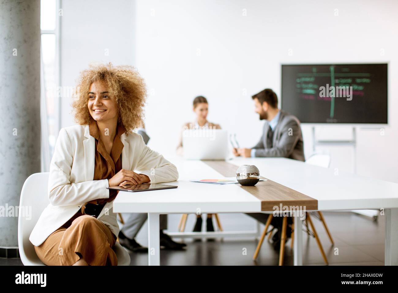 Young curly hair businesswoman using digital tablet in the office with young people works behind her Stock Photo
