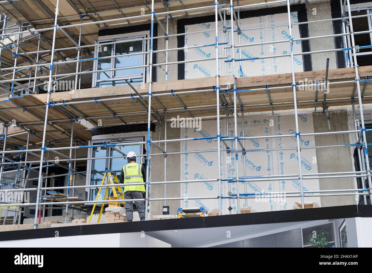 a builder in high viz jacket walk on the plank inside scaffolding in a new development building site Greenwich London England UK Stock Photo