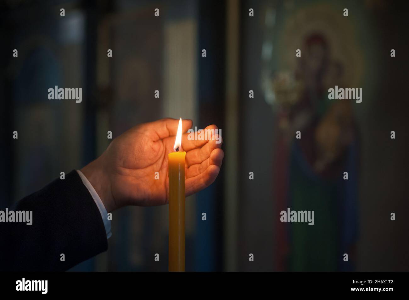Closeup of hands of religious man holding lit candle and praying in the church in the front of
