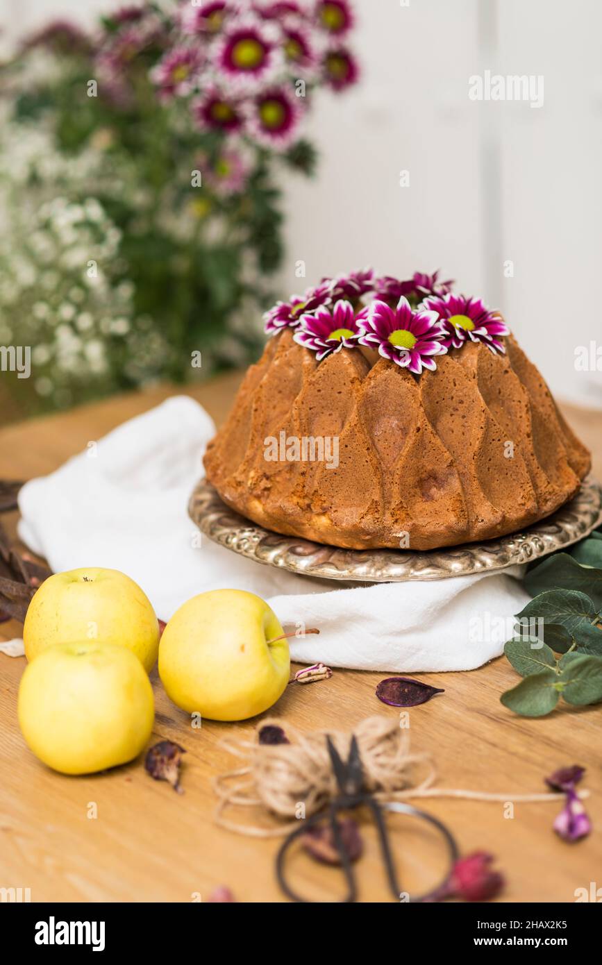 Still life with an apple sponge cake decorated with flowers and kitchen utensils. Stock Photo