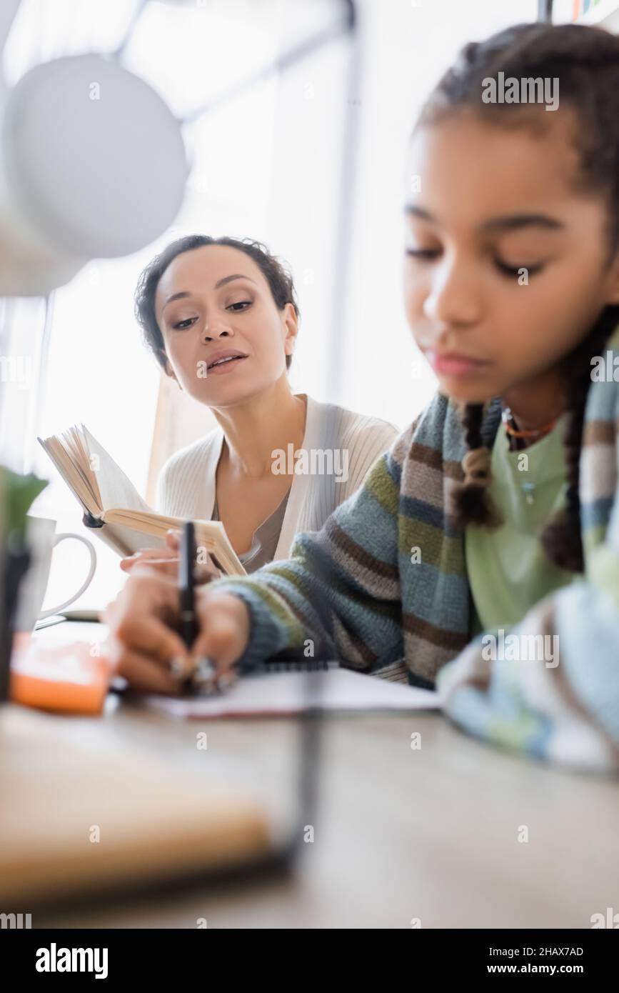 blurred african american teen girl writing in notebook near mother with book Stock Photo