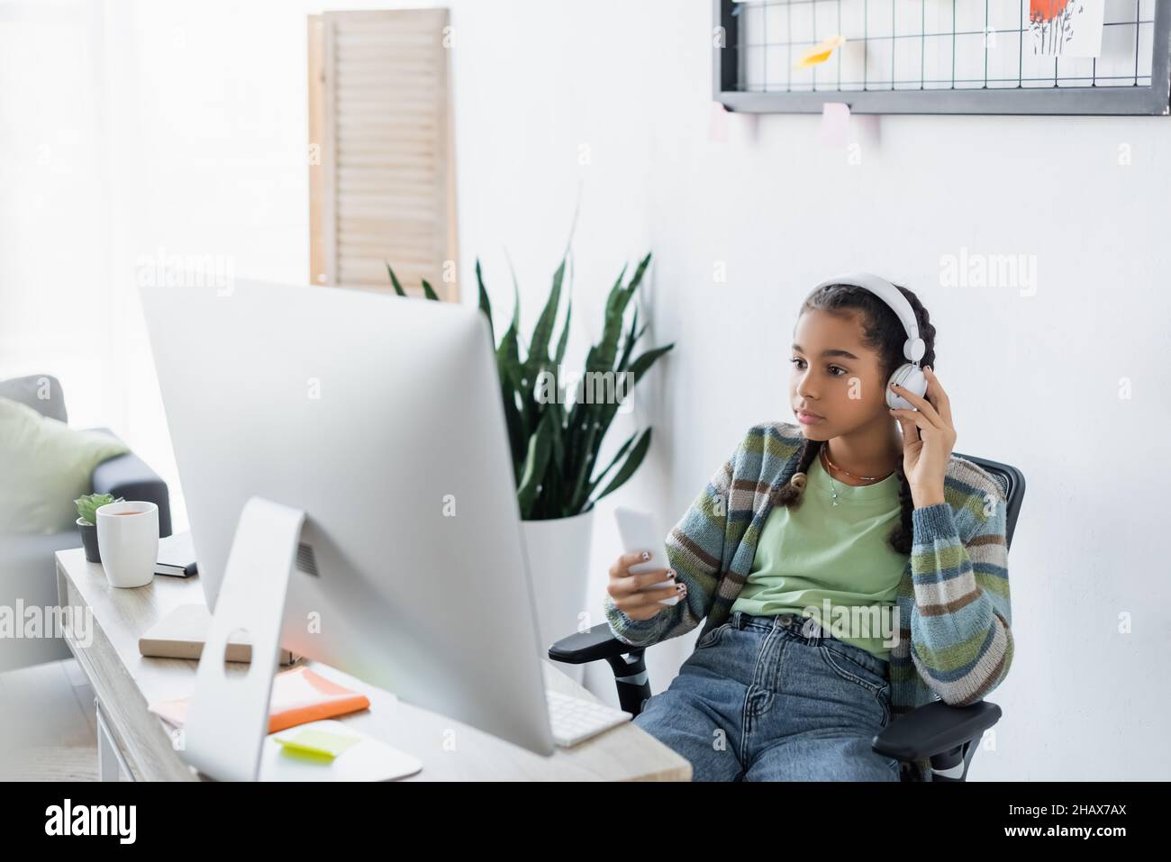 african american teen girl holding cellphone while sitting near computer monitor Stock Photo