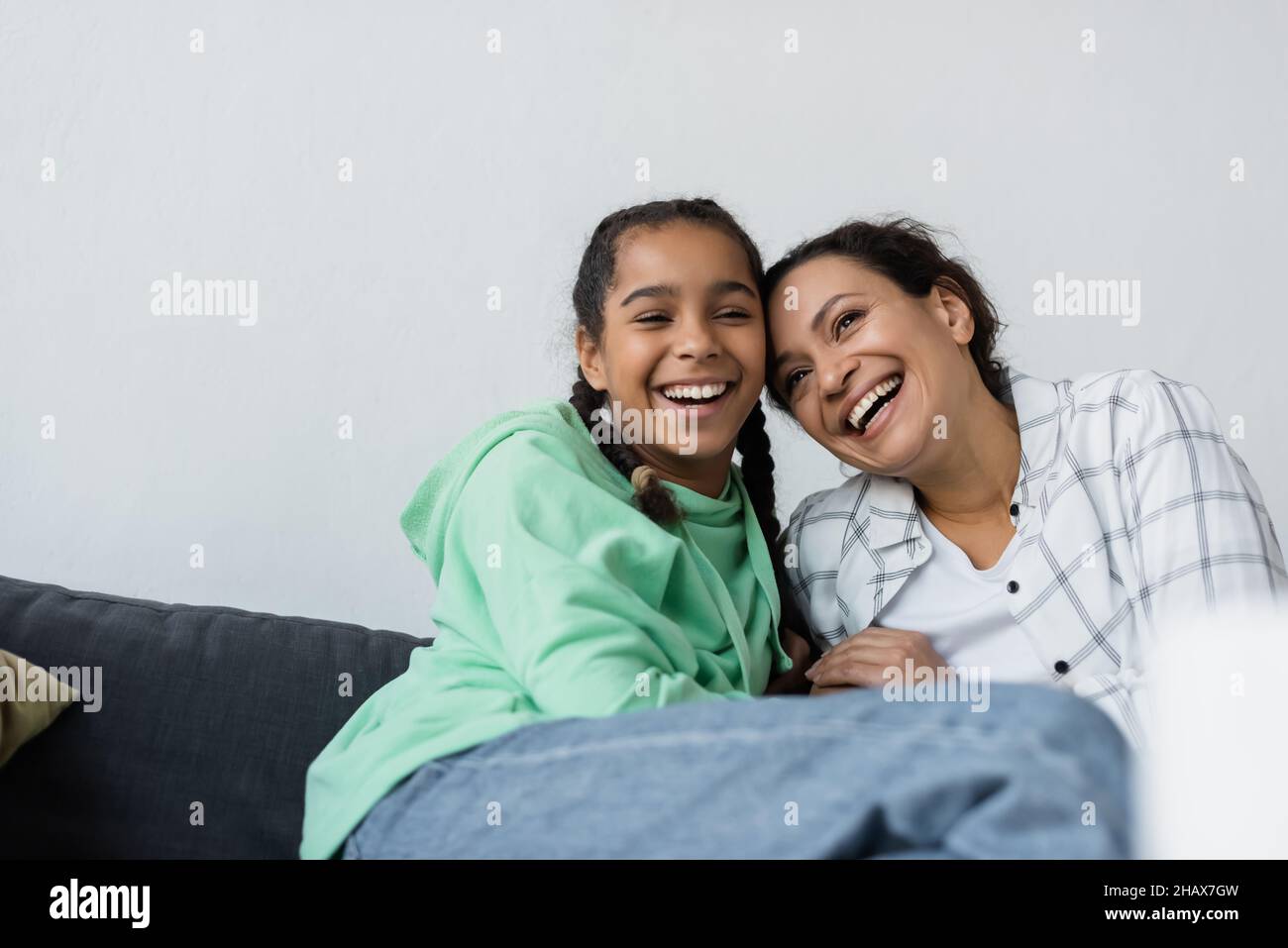 excited african american mother and daughter laughing on sofa at home Stock Photo