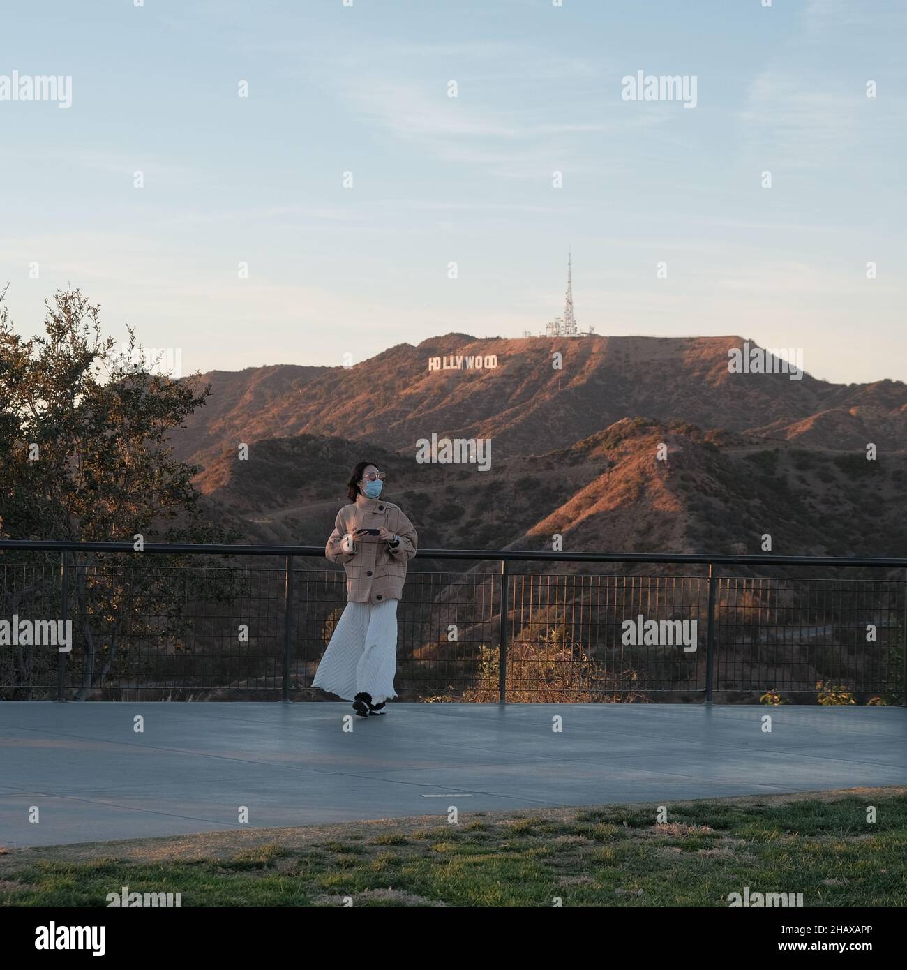 LOS ANGELES, UNITED STATES - Jun 12, 2019: A young female tourist leaning against a fence with the Hollywood Sign on Mount Lee in the background Stock Photo