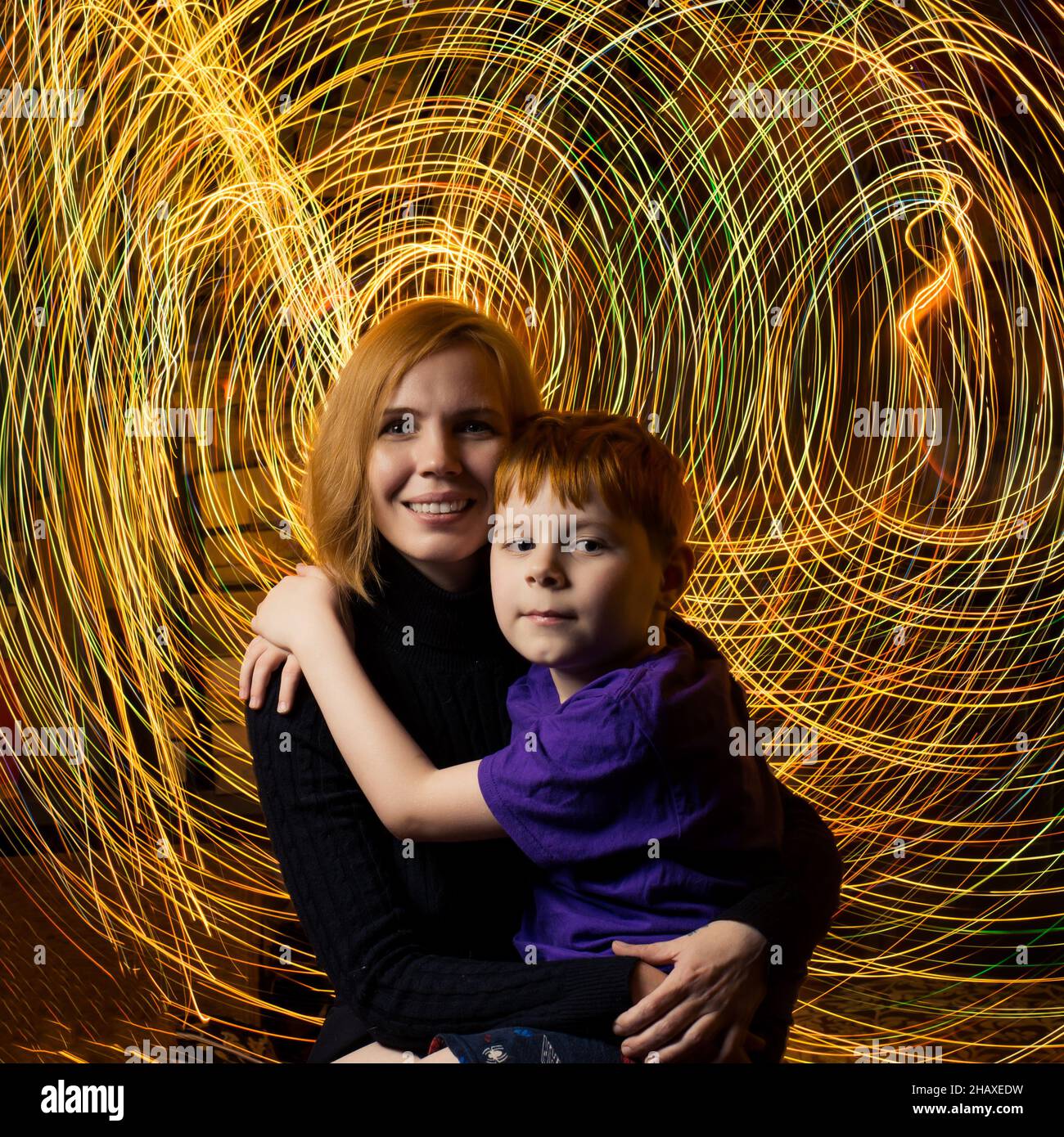 A woman hugs a child on a background of rays of energy in the dark. Mother and son unity concept. Stock Photo