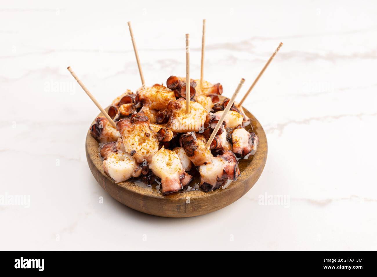 Galician style octopus in wooden plate on marble table. Typical appetizer of Galicia, Spain. Pulpo a Feira Stock Photo