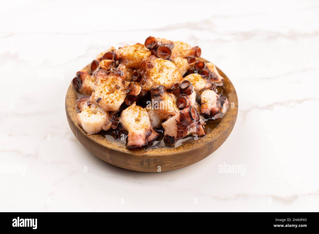 Galician style octopus in wooden plate on marble table. Typical appetizer of Galicia, Spain. Pulpo a Feira Stock Photo