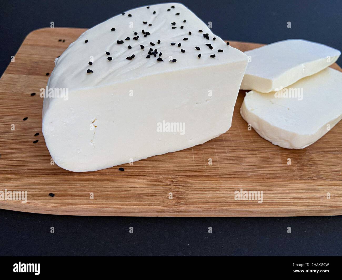 White cheese, cheese slices on a wooden plate with black background. Stock Photo