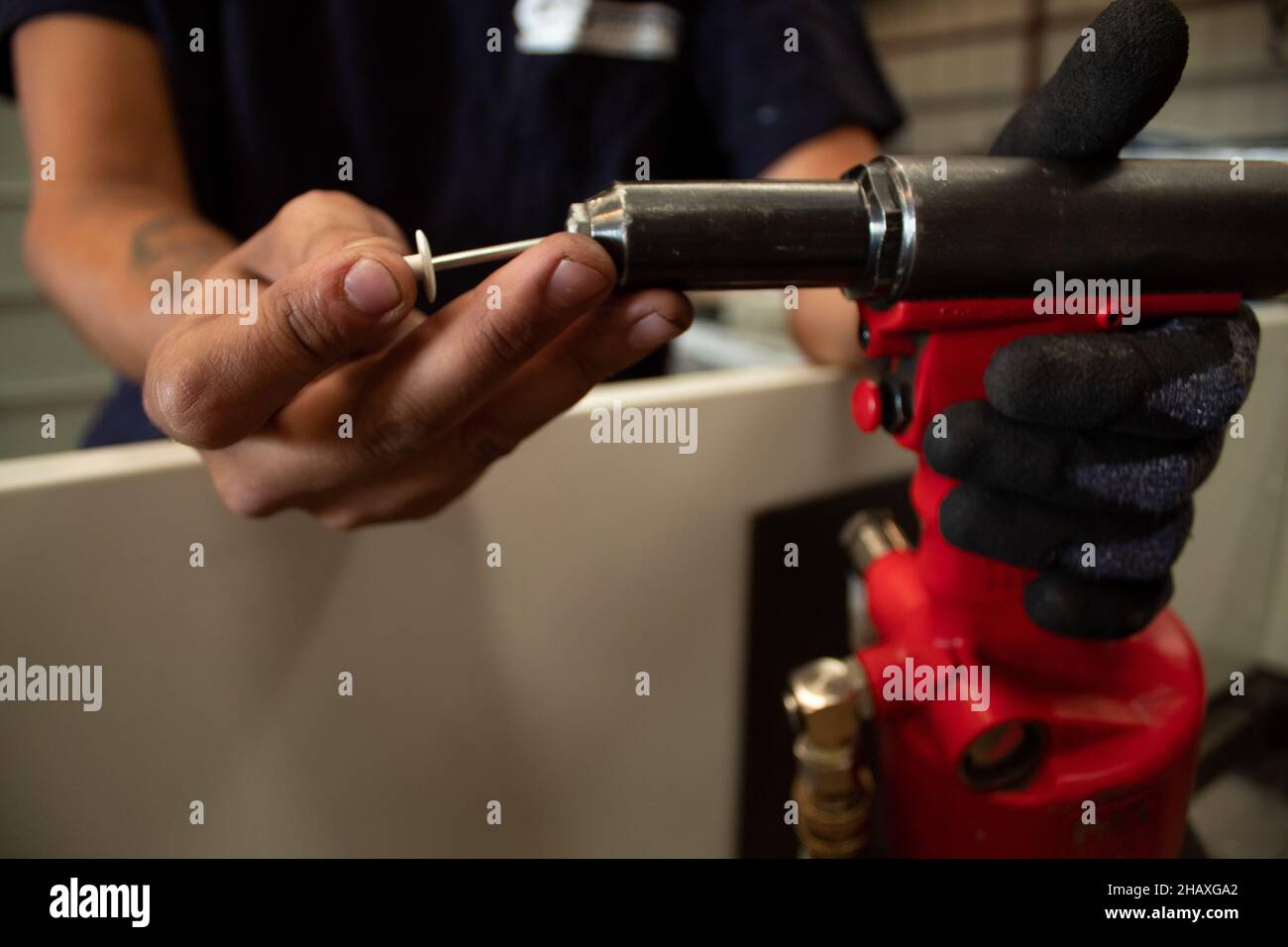 Worker uses a rivet hand gun, and inserts a rivet into it. Manual rivet