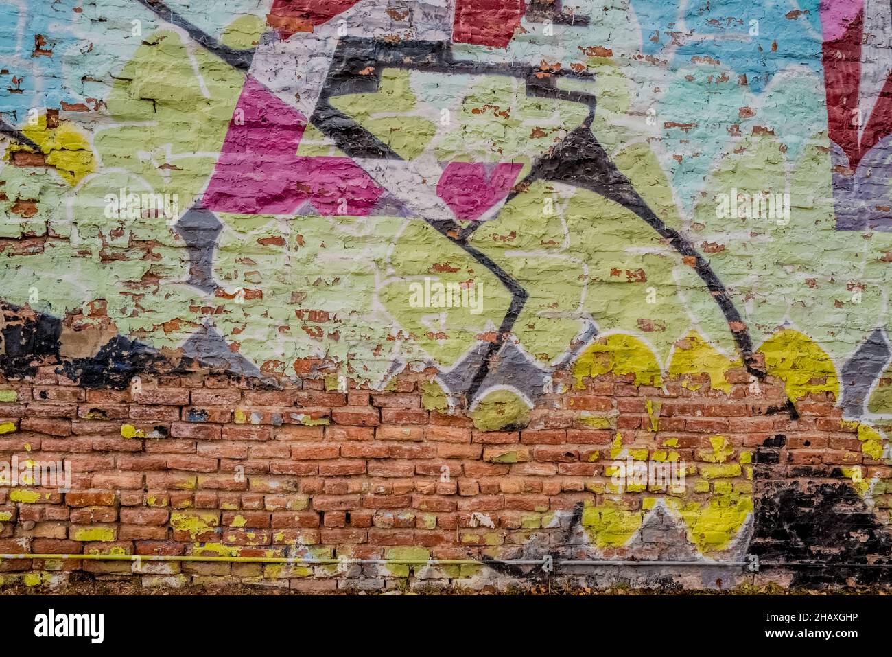 Colorful close up of graffiti on a brick and concrete wall including colors mainly of black pink and green and unpainted bricks. Stock Photo