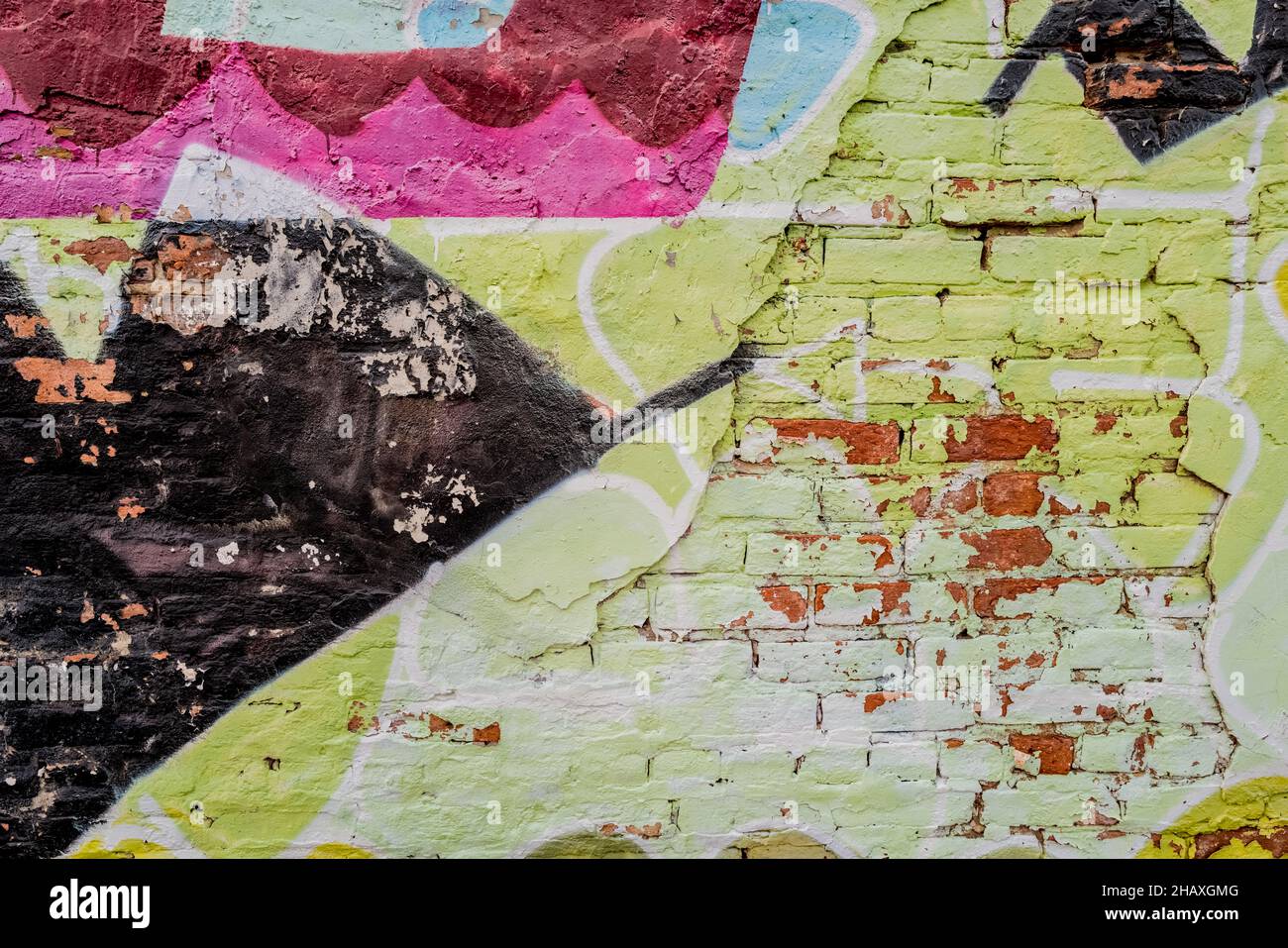 Colorful close up of graffiti on a brick and concrete wall including colors mainly of black pink and green. Stock Photo