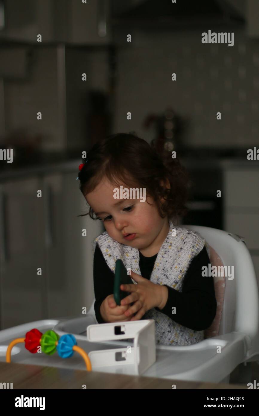 Baby girl with telephone, baby struggles with technology. Kitchen background and selective focus. Generation Z concept and idea. Stock Photo