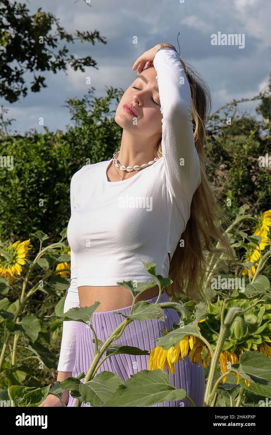 Beautiful teenage girl standing in a sunflower field playing with her hair, France Stock Photo