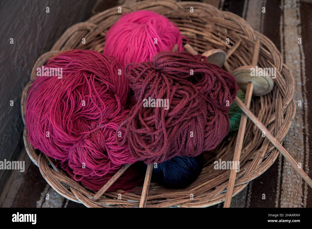 Dyed alpaca llama wool in balls with traditional knitting needles resting in wicker bowl basket at peruvian textile farm for tourists to see ancient m Stock Photo