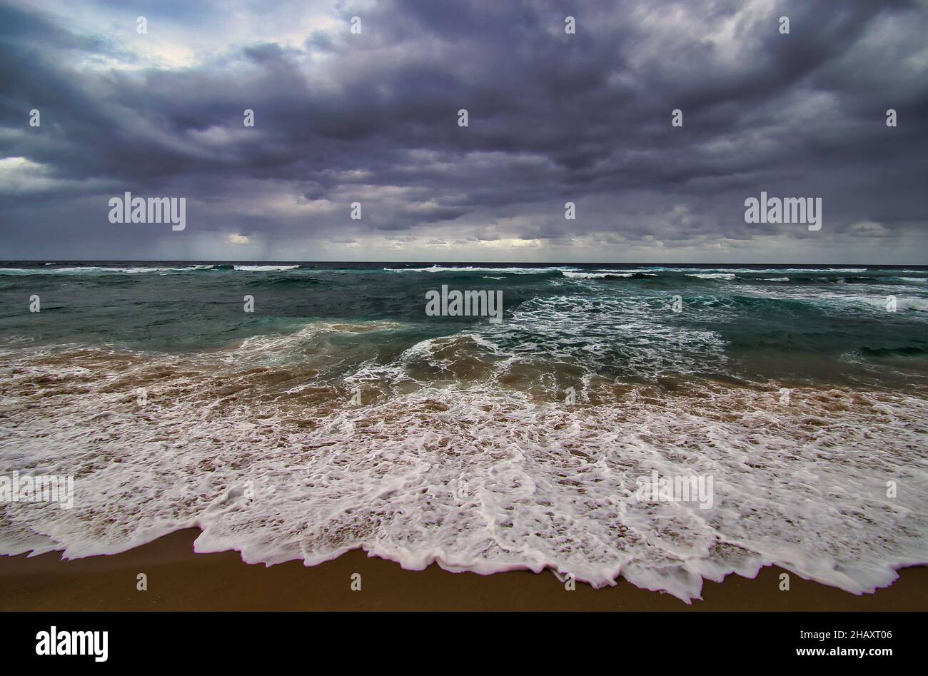 Foamy waves of the Indian Ocean crashing on the sandy beach under a ...