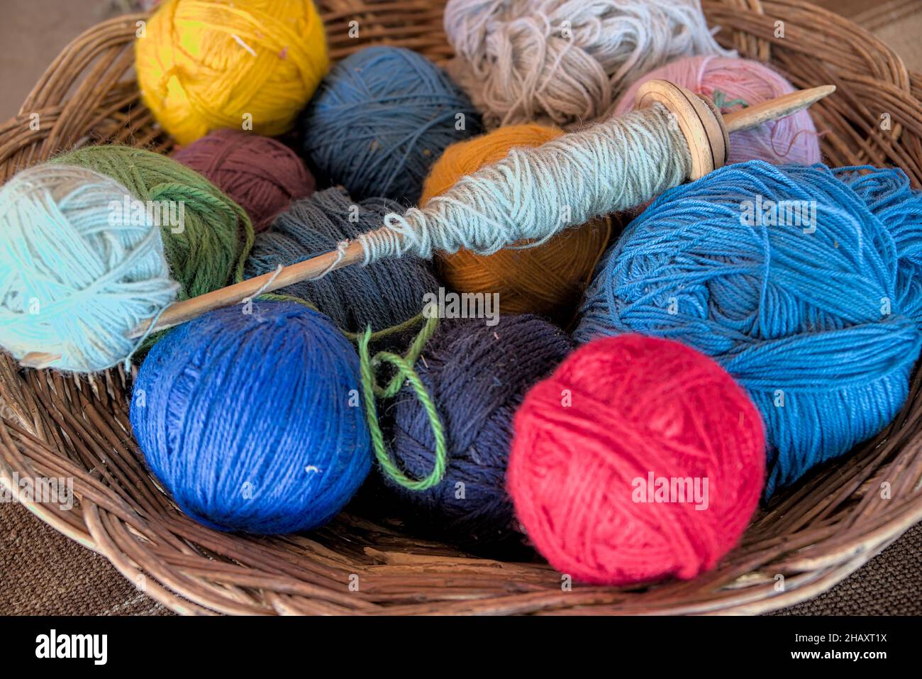 Dyed alpaca llama wool in balls with traditional knitting needles resting in wicker bowl basket at peruvian textile farm for tourists to see ancient m Stock Photo