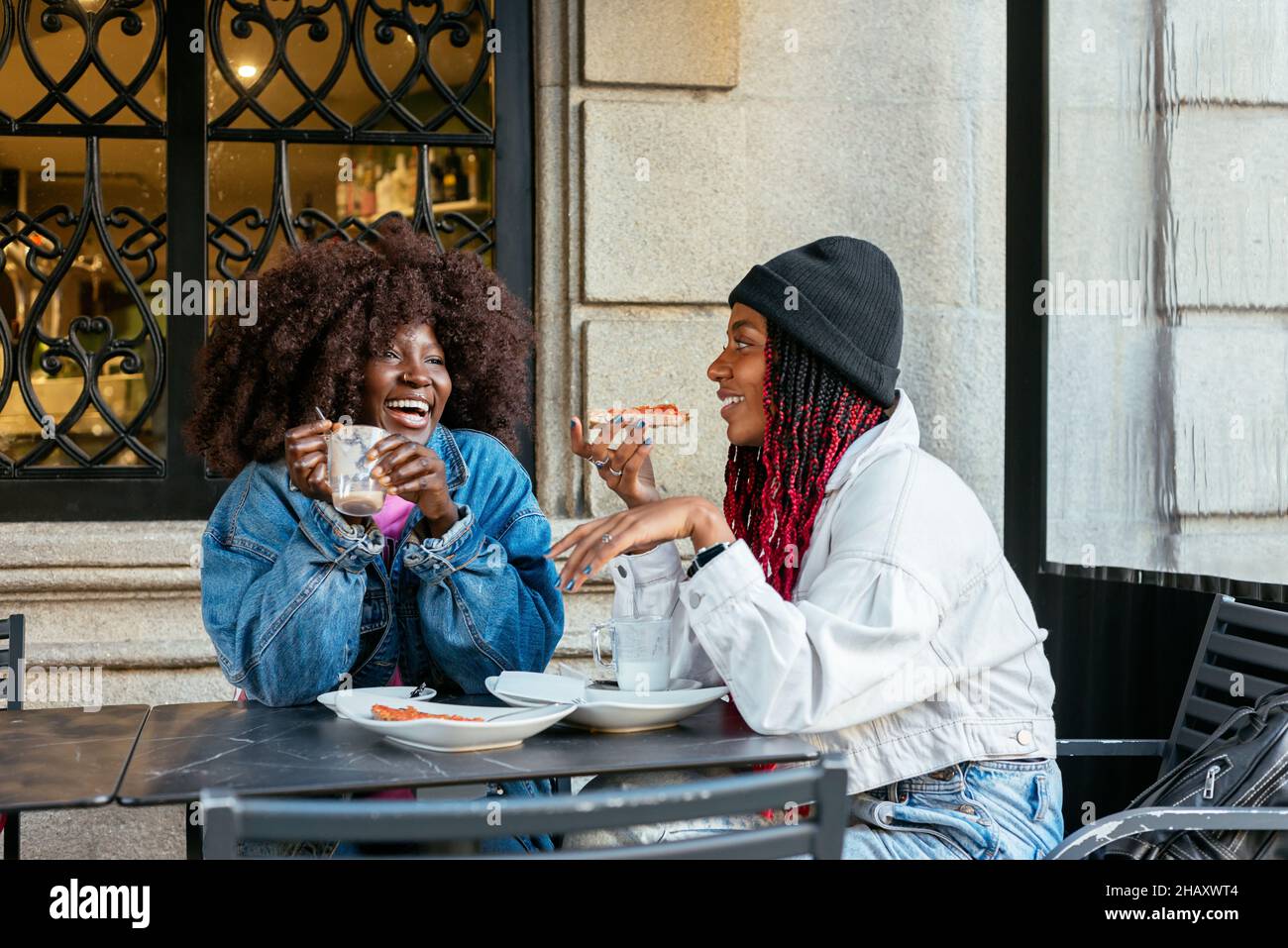 Happy African American women looking at each other while sitting at table and eating tasty lunch in outdoor cafe Stock Photo