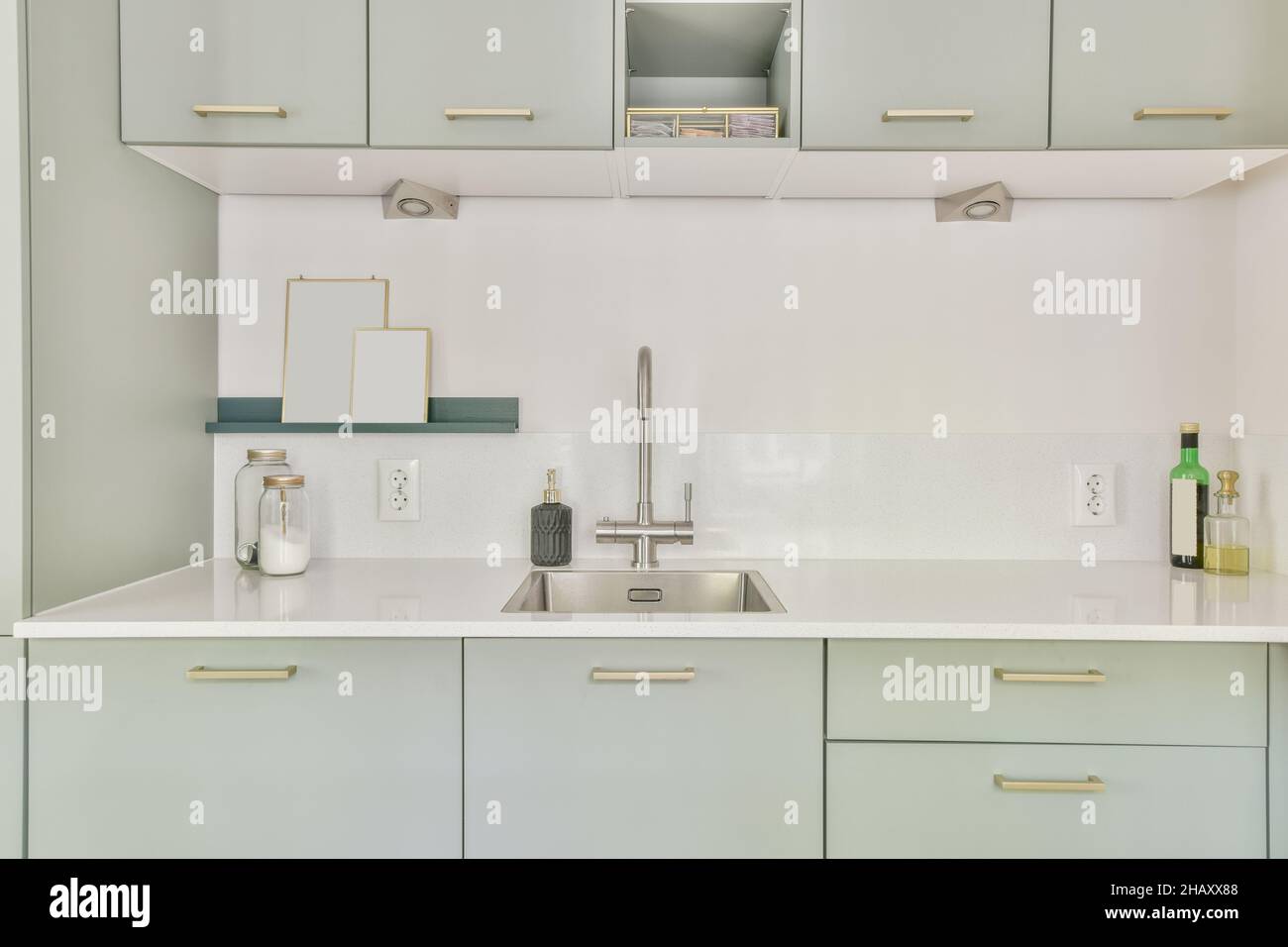 Interior of modern kitchen with light green cupboards and cabinets sink with faucet and metal ...
