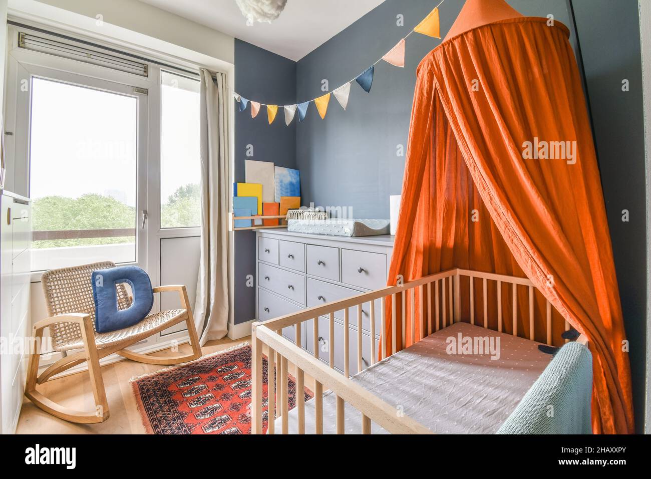 Baby crib with orange canopy placed near white drawers and