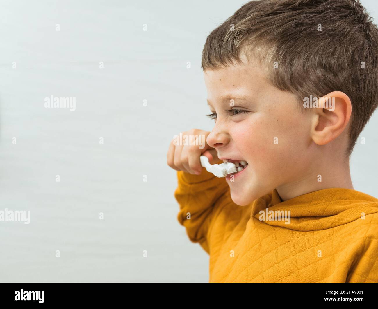 Cute boy in casual wear brushing teeth in bathroom during morning ...