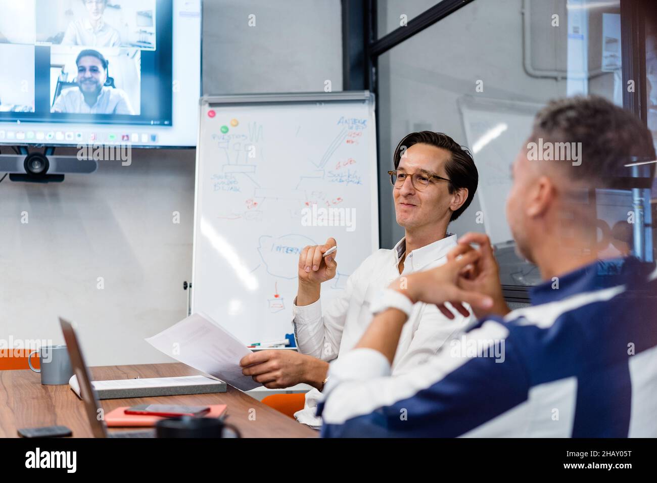 Coworkers sitting at table with gadgets and documents in modern workspace with white flip chat during online conference in office Stock Photo