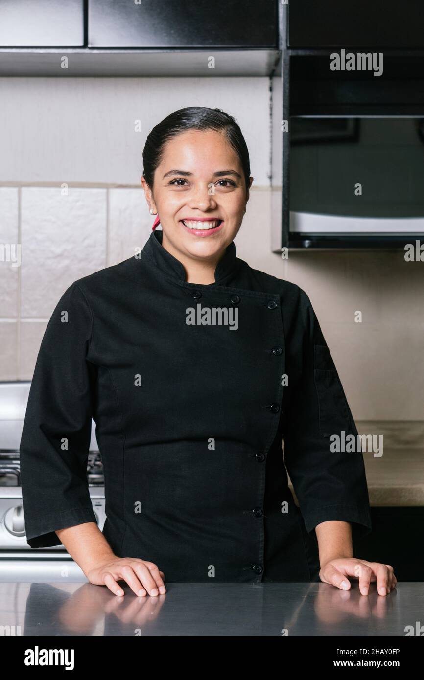 Smiling ethnic female chef in black professional uniform standing at metal  table in modern kitchen in restaurant Stock Photo - Alamy