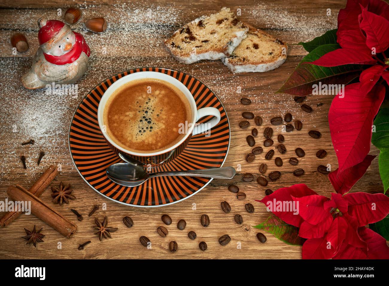 Weihnachtliches Kaffeemotiv mit Kaffeetasse, Weihnachtsstern, Stollen, Kaffeebohnen, Gewürzen, Haselnüssen und einer Vogelfigur auf einem Holztisch. Stock Photo
