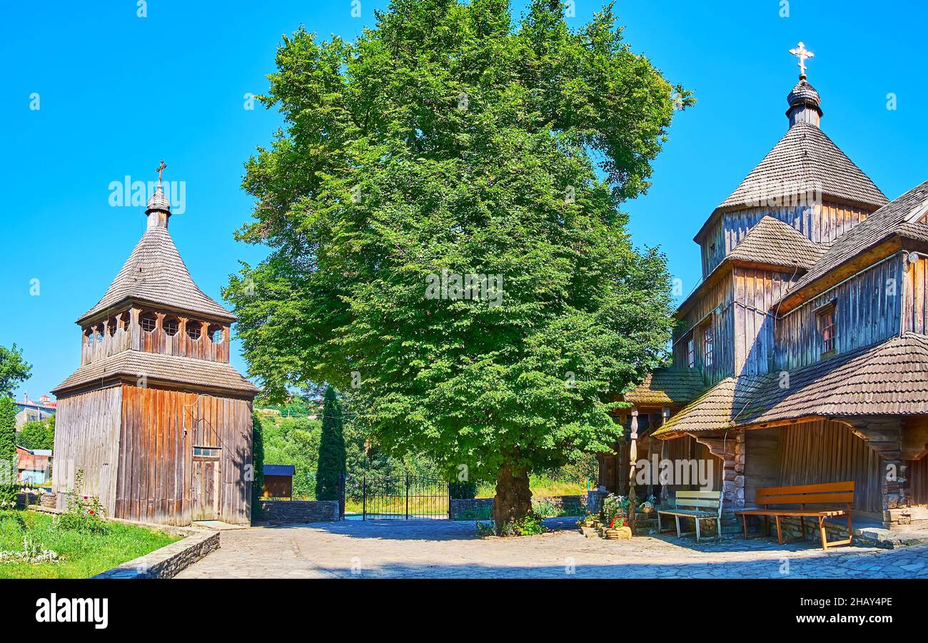 The tall spread linden, growing next to the old timber Zdvyzhenska (Exaltation of Holy Cross) Church and it's separate belfry, Kamianets-Podilskyi, Uk Stock Photo