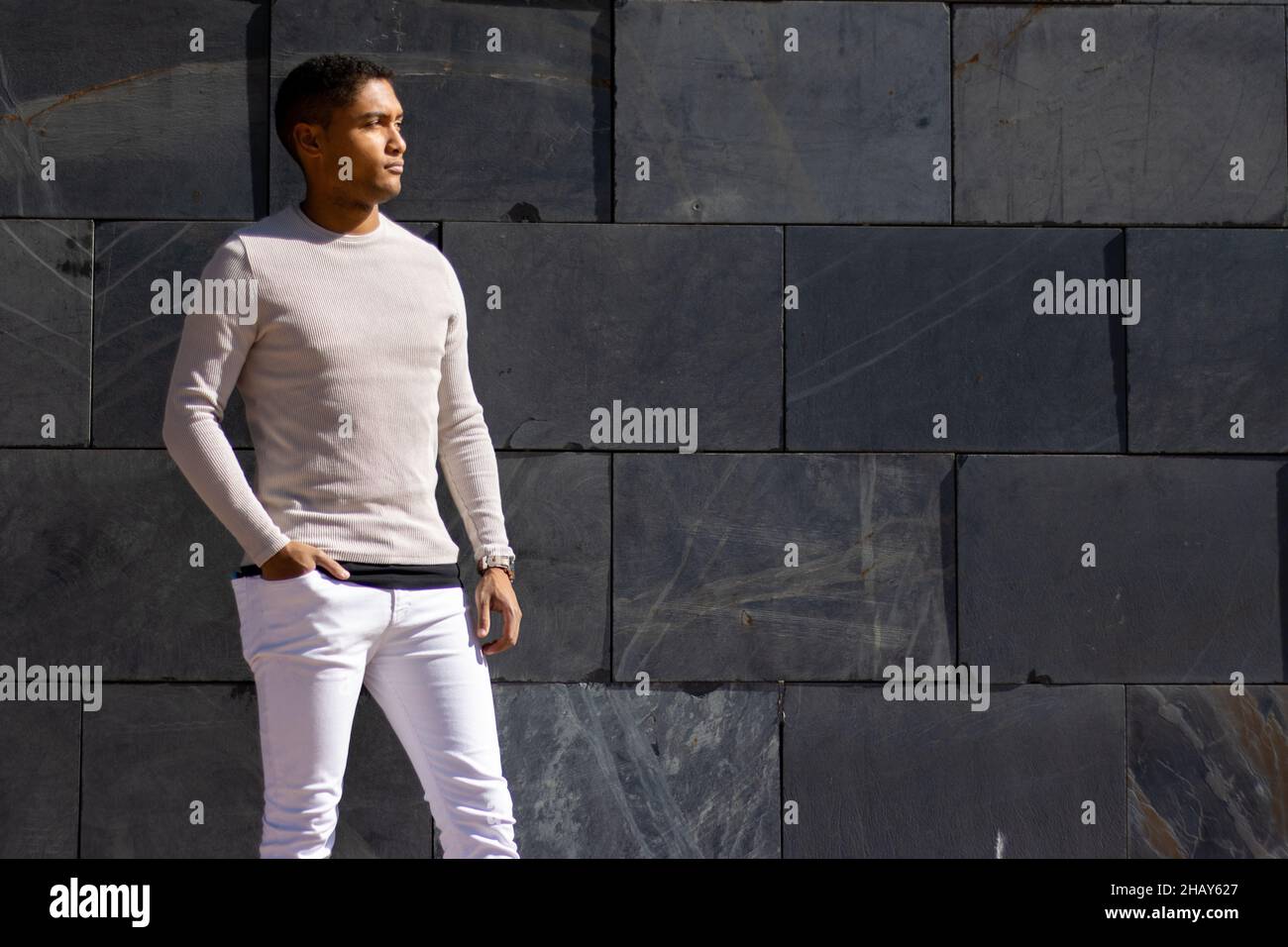 Man posing in trousers and a white pullover with a flagstone background Stock Photo