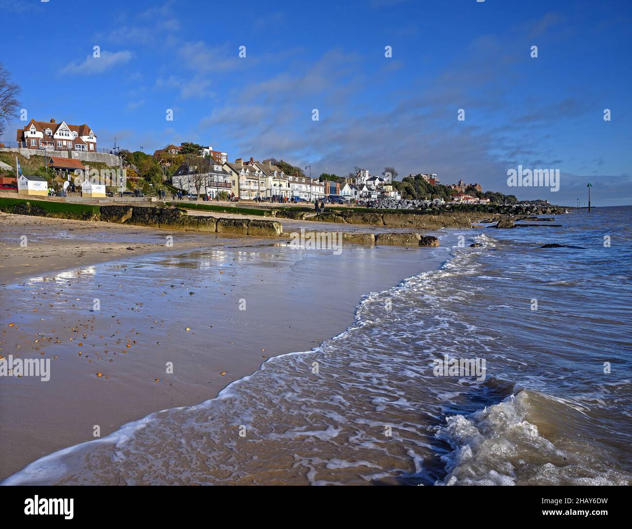 Felixstowe, Suffolk, UK: Waves lap against the sandy beach in the English resort town of Felixstowe. People walk along the promenade and beach. Stock Photo