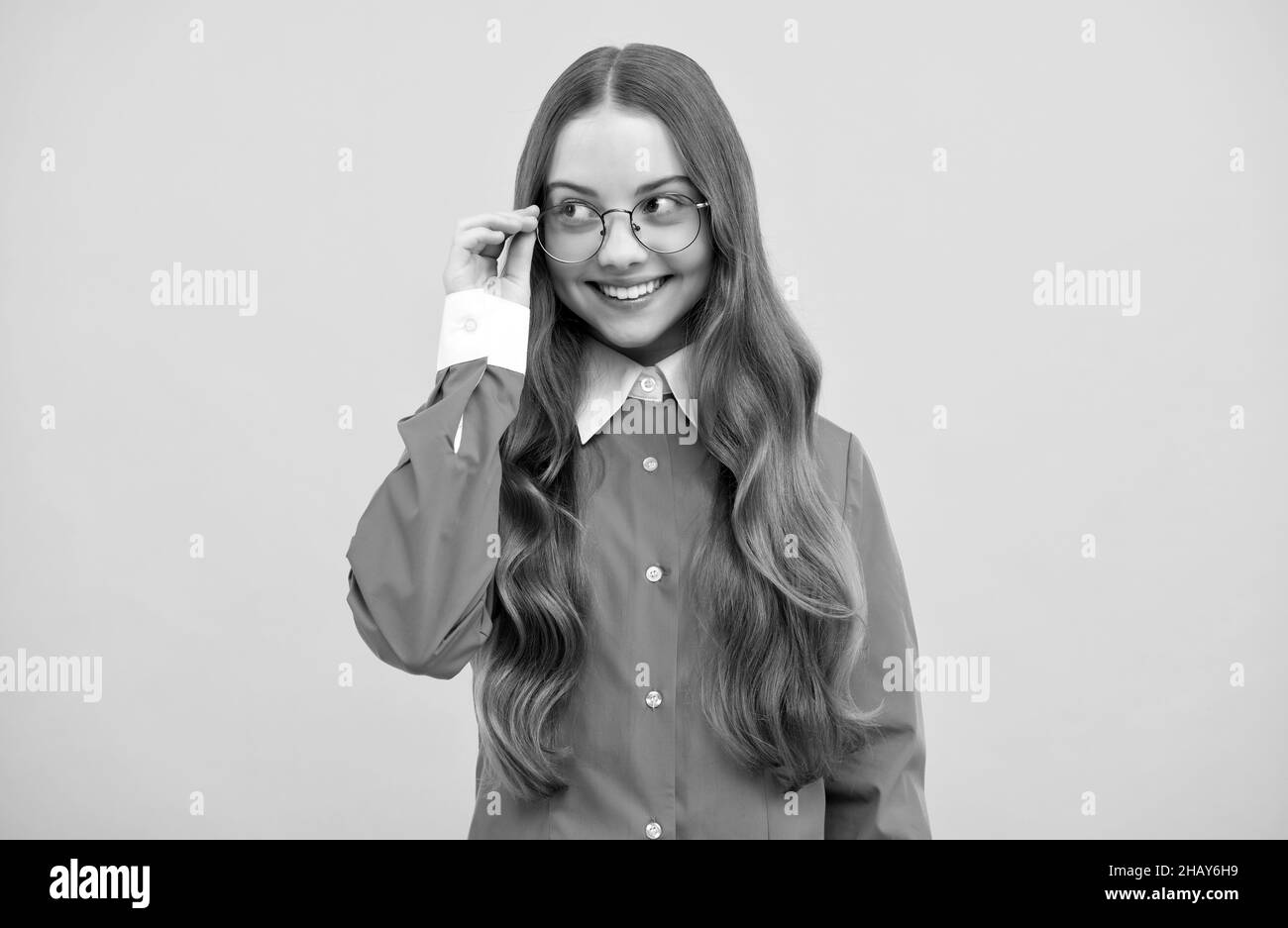 Happy teenage school girl fix eyeglasses smiling yellow background, eyewear Stock Photo