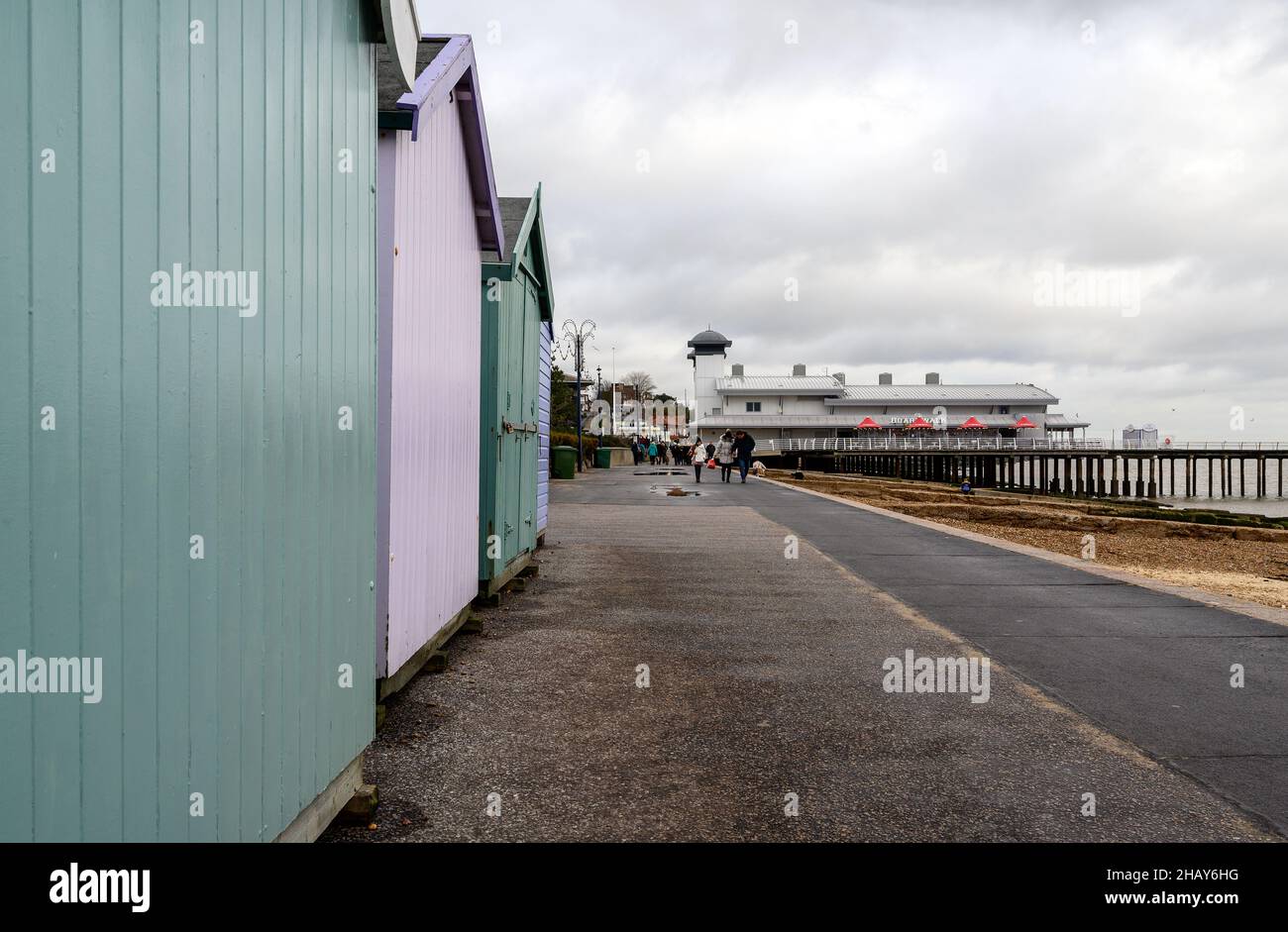 Felixstowe, Suffolk, UK:  People walk along Felixstowe promenade on a cold and dull winter's day past a line of beach huts and the pier. Stock Photo