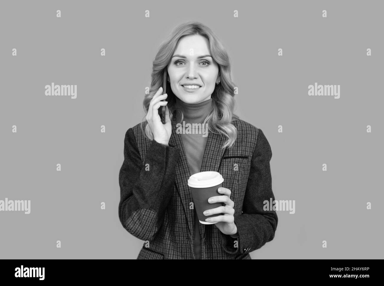 Happy woman talk on mobile phone drinking morning coffee grey background, talker Stock Photo