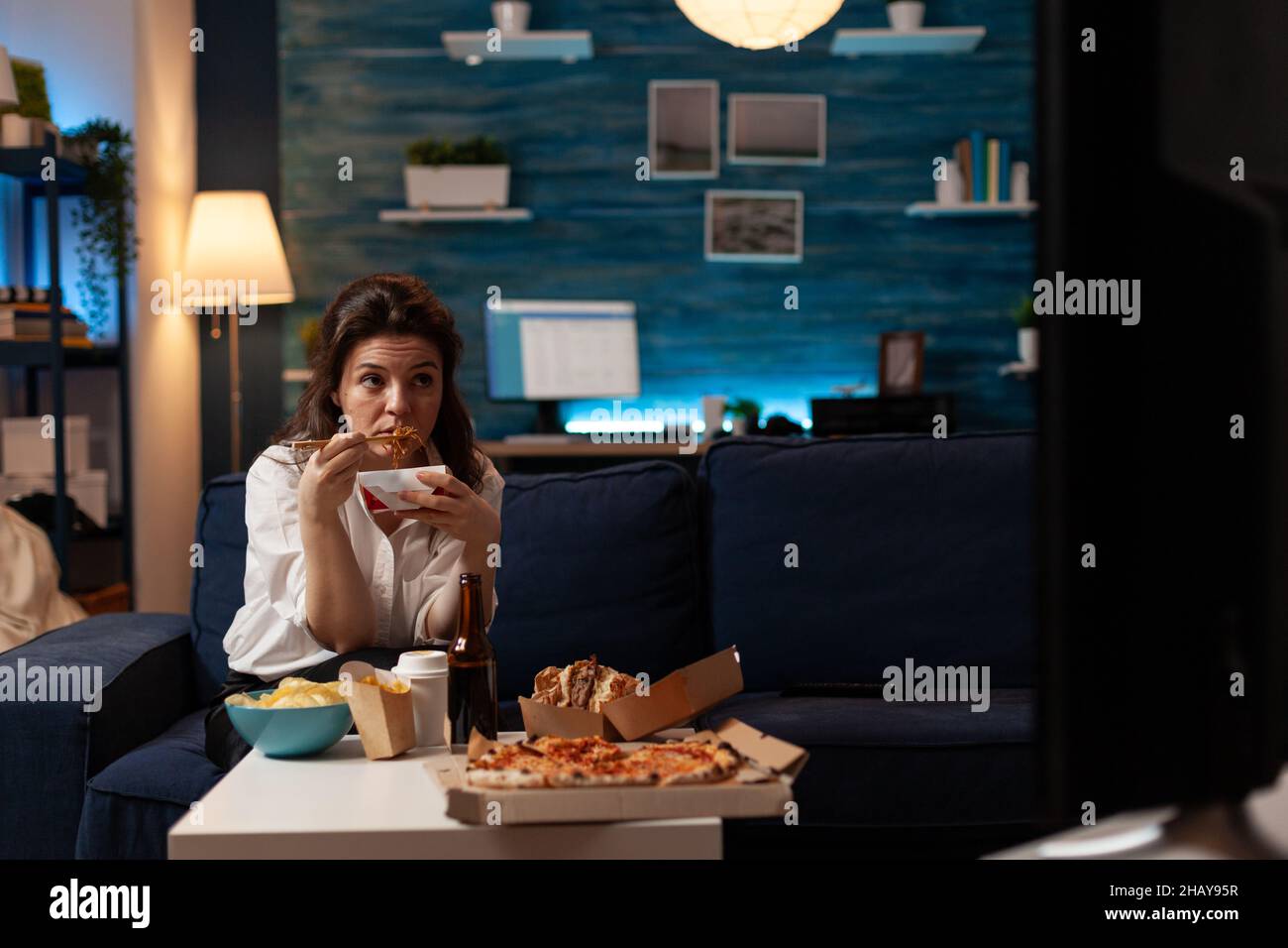 Woman sitting on couch eating takeout asian noodles with chopsticks
