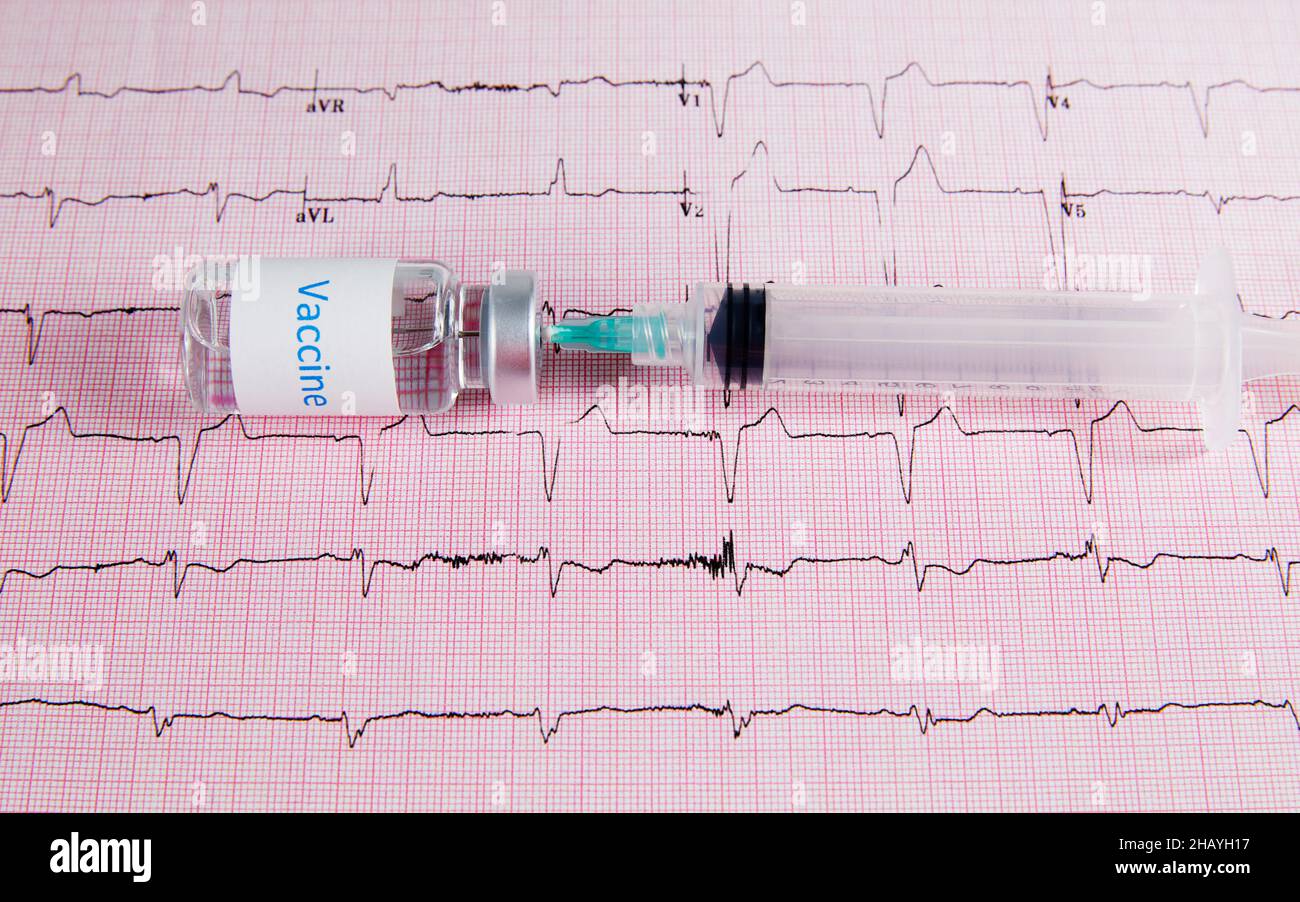 A vaccine bottle with a hypodermic needle and syringe laying on top of a heart monitor graph or echocardiograph printout. Stock Photo