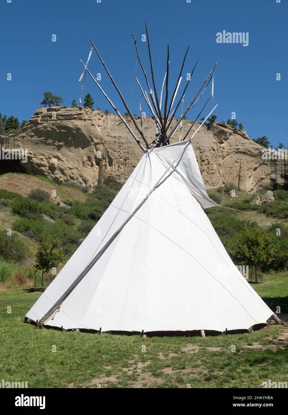 White canvas teepee or tipi in a field at Pictograph Cave State Park near Billings, Montana, with a sandstone cliff and cave in the background and dee Stock Photo