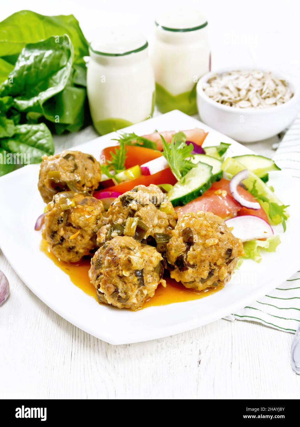 Minced meatballs with spinach, oatmeal and green onions in tomato sauce, vegetable salad in a plate, napkin on a wooden board background Stock Photo