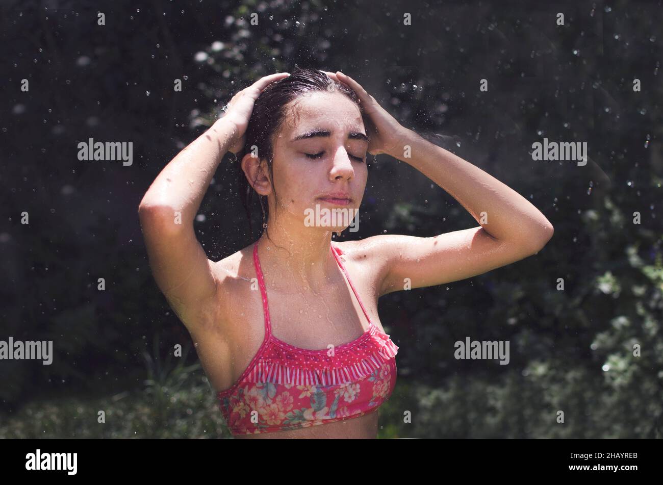 Teenage girl standing in a garden cooling off with a water hose, Argentina Stock Photo