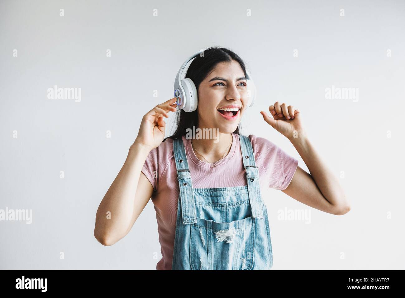 Portrait of latin young smiling woman with headphones, dancing and listening to music on a white background in Latin America Stock Photo