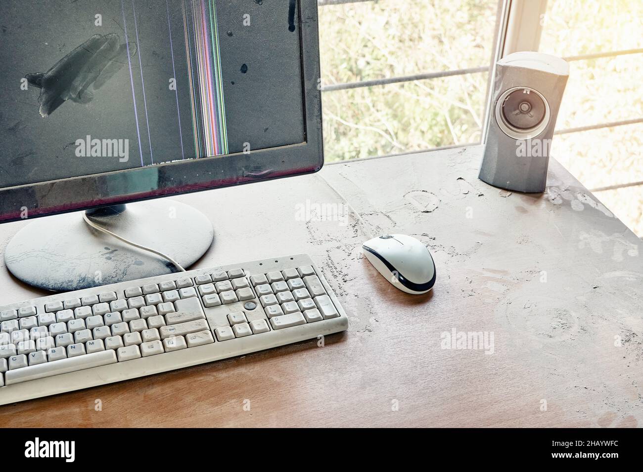 Old keyboard with mouse and broken monitor with audio speaker are on wooden table and covered in thick dust in a workshop Stock Photo