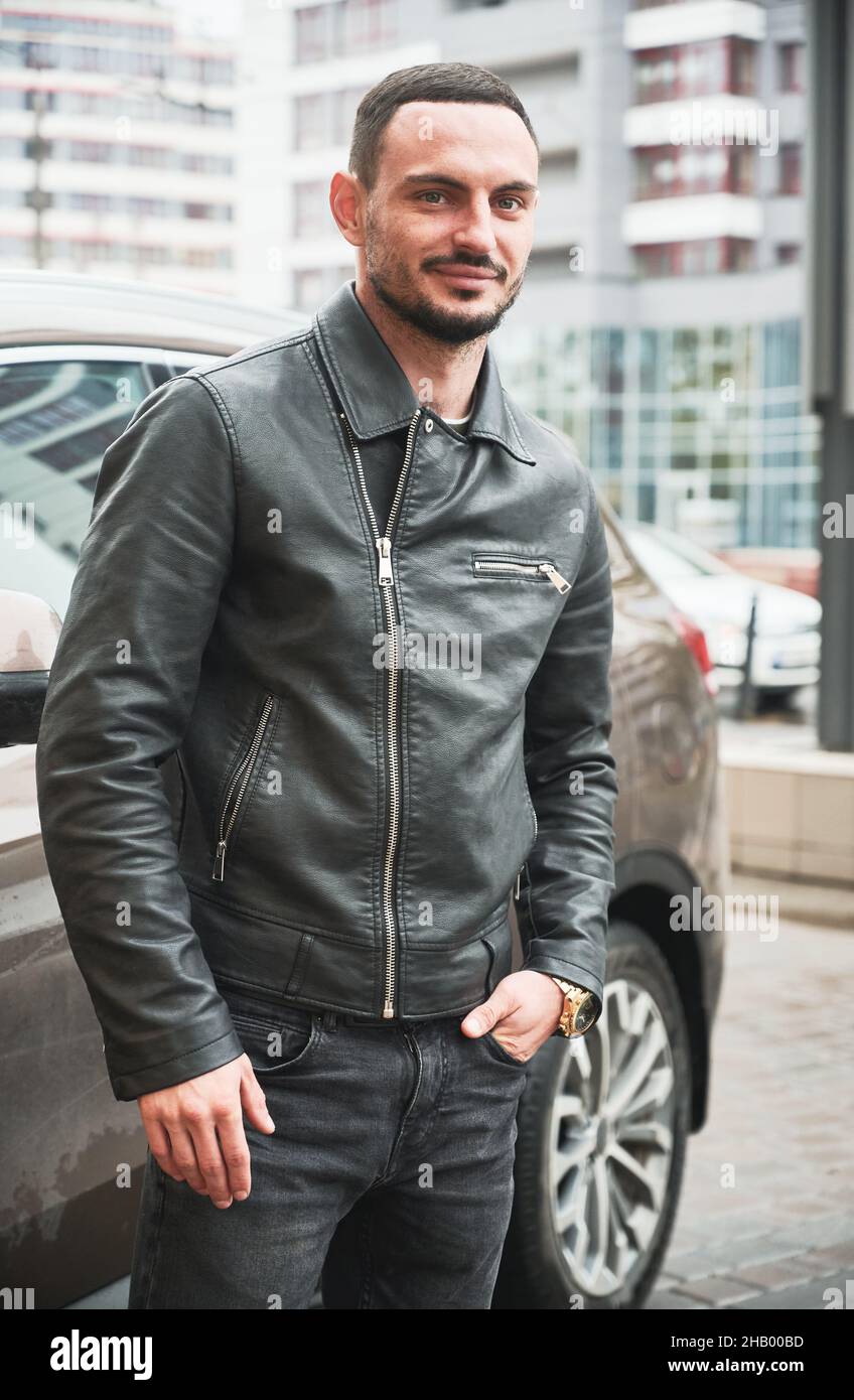 Portrait of handsome young man posing near his modern car outdoor. Guy wearing casual clothes and gold watch. Stock Photo