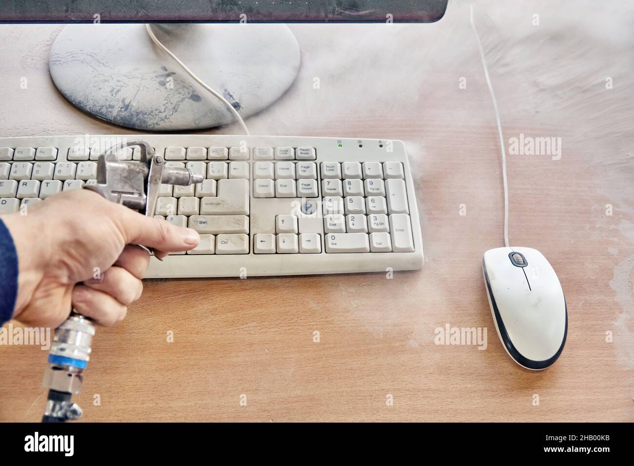 Employee cleans a dusty keyboard and dusty desk with air duster cleaning spray gun in the