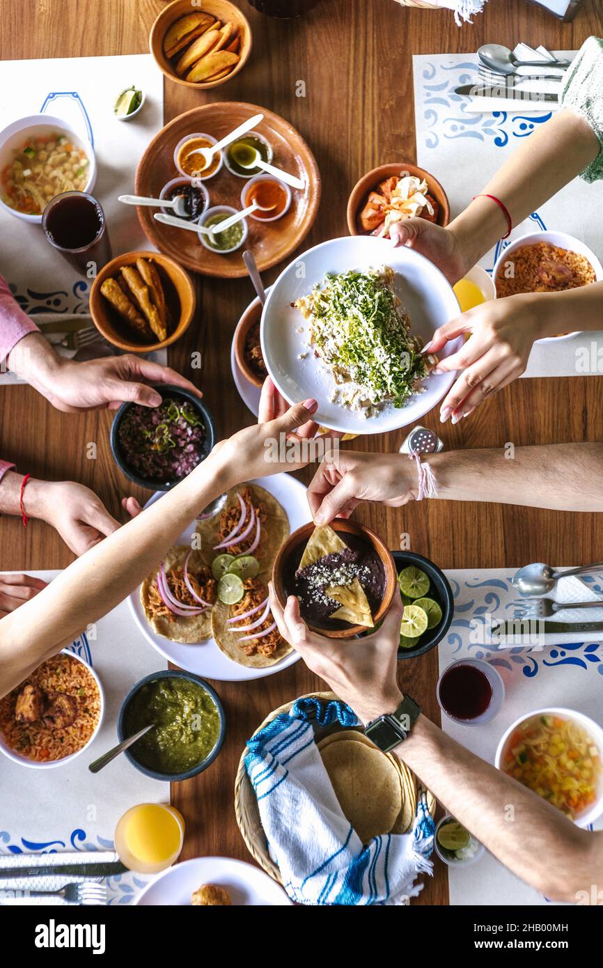 Group of latin friends eating mexican tacos and traditional food, snacks and people's hands over table, top view. Mexican cuisine Latin America Stock Photo