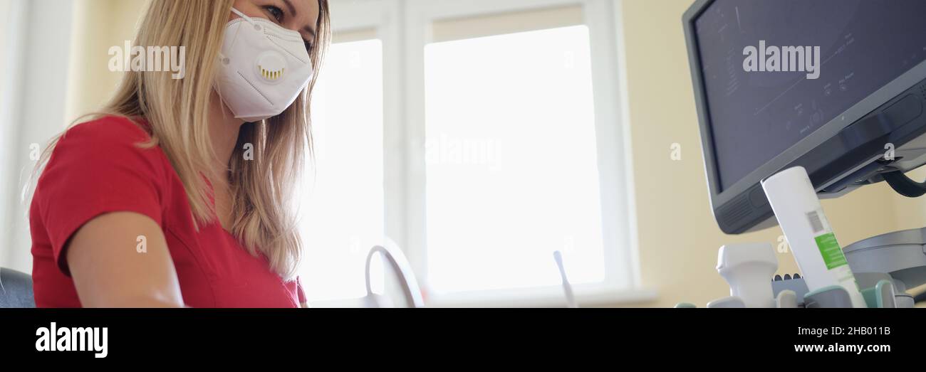 Doctor in medical protective mask doing ultrasound examination of abdominal cavity to patient in clinic Stock Photo