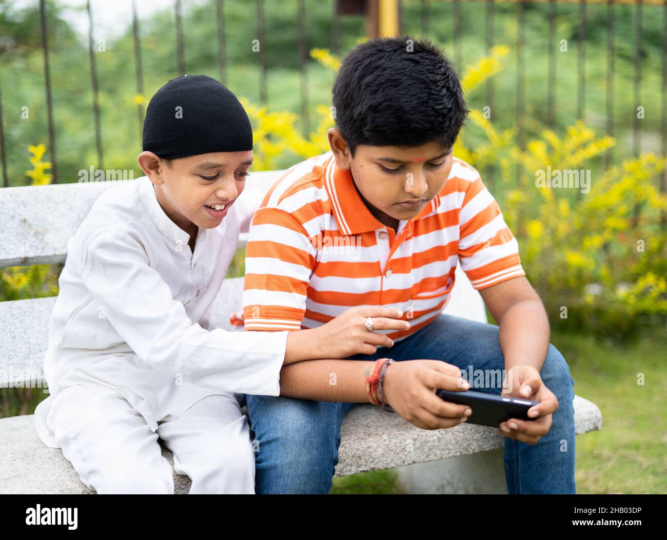 Mutiethnic kids playing video game on mobile phone at park - concept of technology, smartphone addiction, friendship and leisure activities Stock Photo