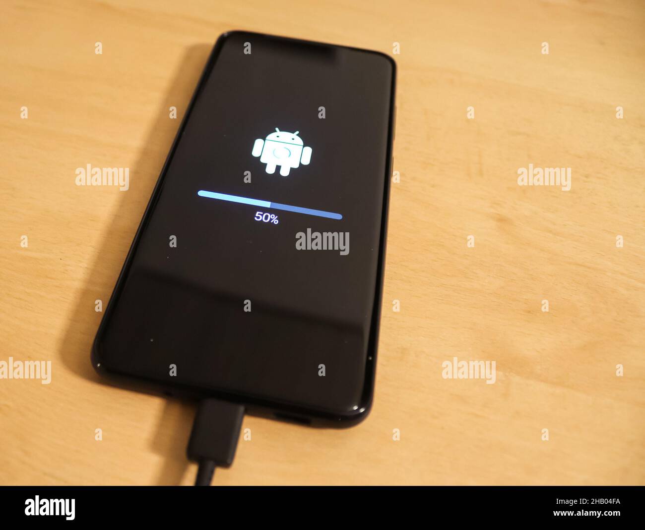 KIEL, GERMANY - Nov 13, 2021: A smartphone on a wooden surface with the progress indicator of an Android operating system update Stock Photo