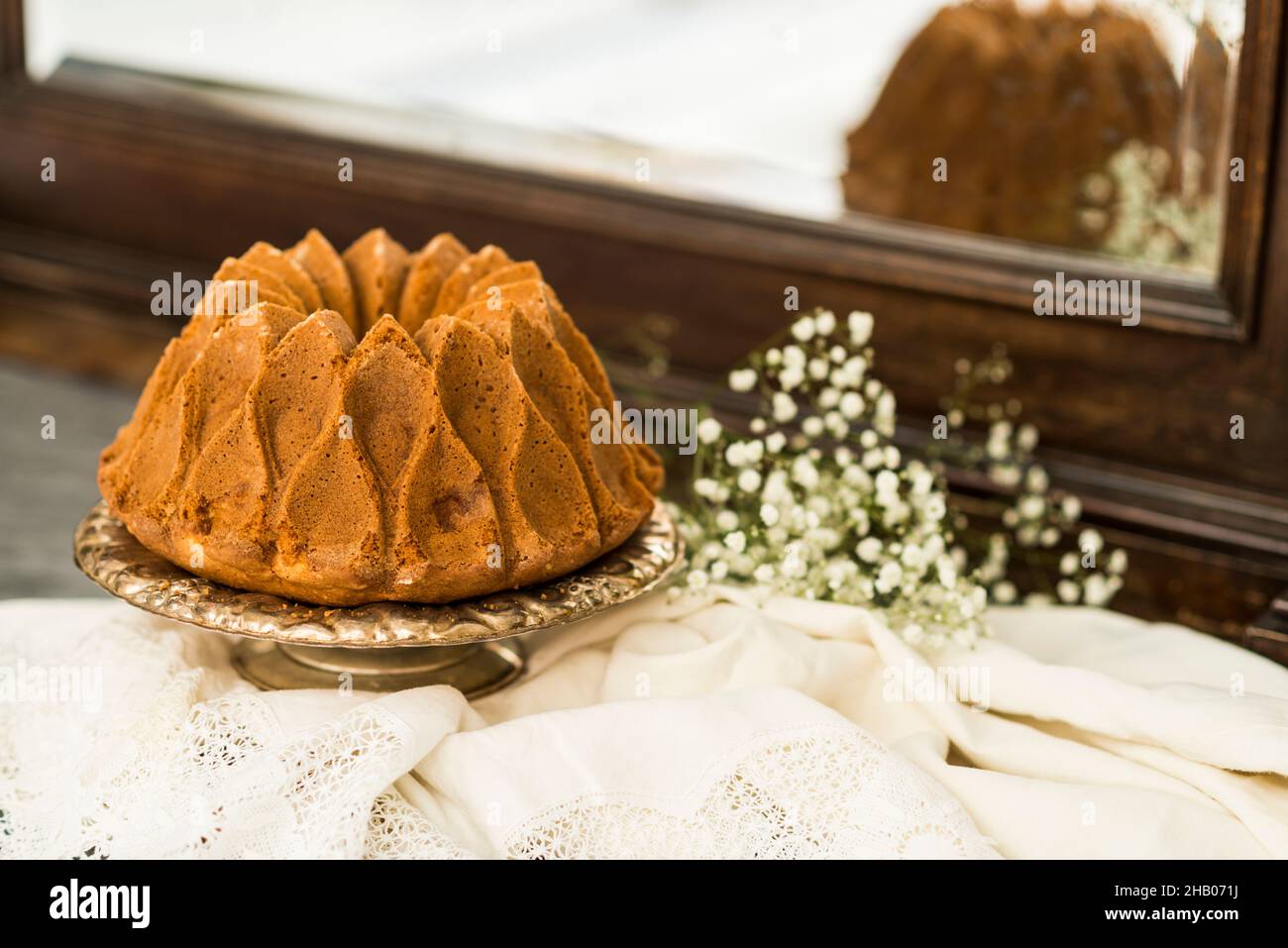 Still life with an apple sponge cake decorated with flowers and kitchen utensils, with a mirror in the background. Stock Photo